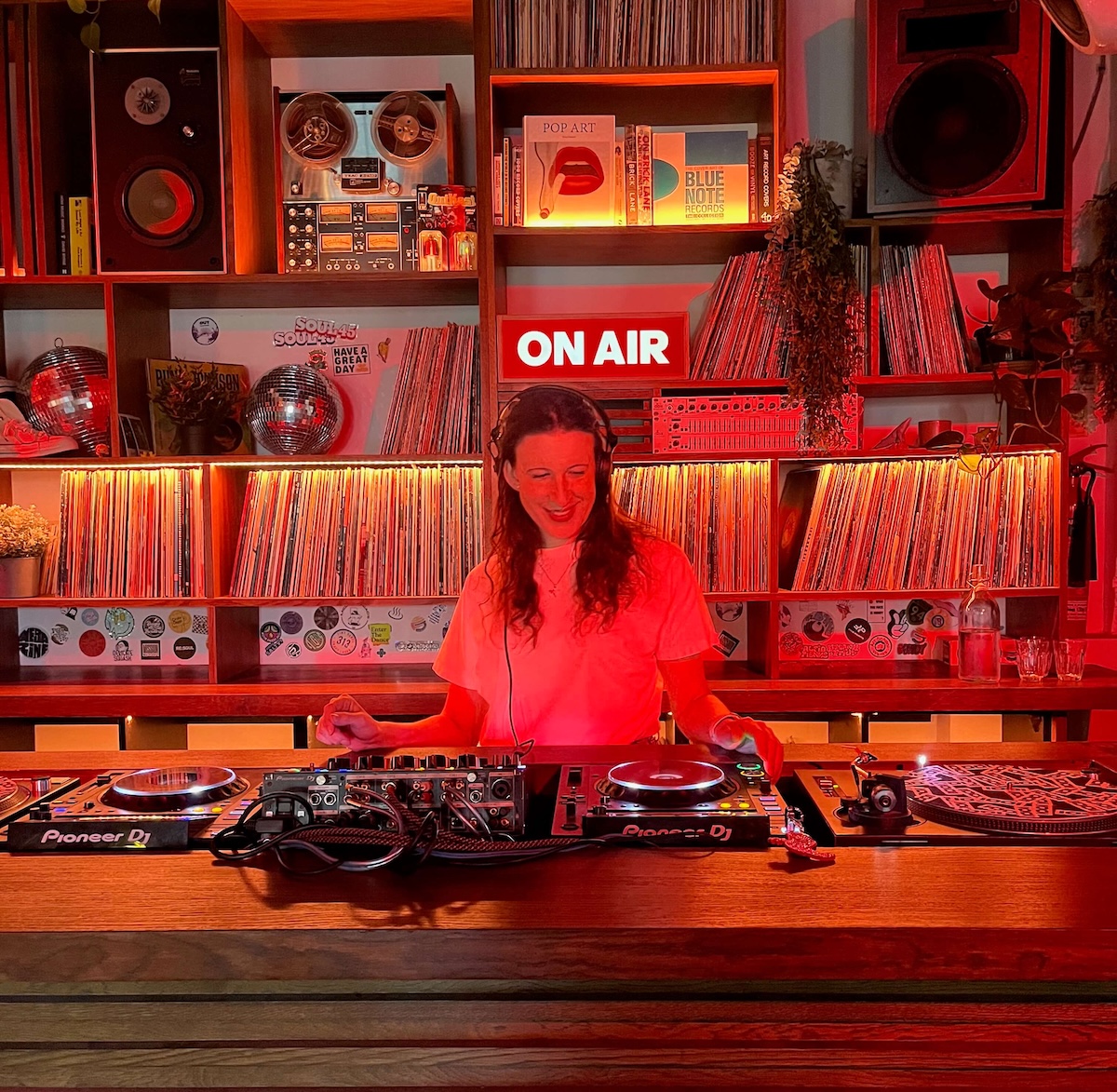 Photo of Zoe in a DJ booth with wooden sheving behind her